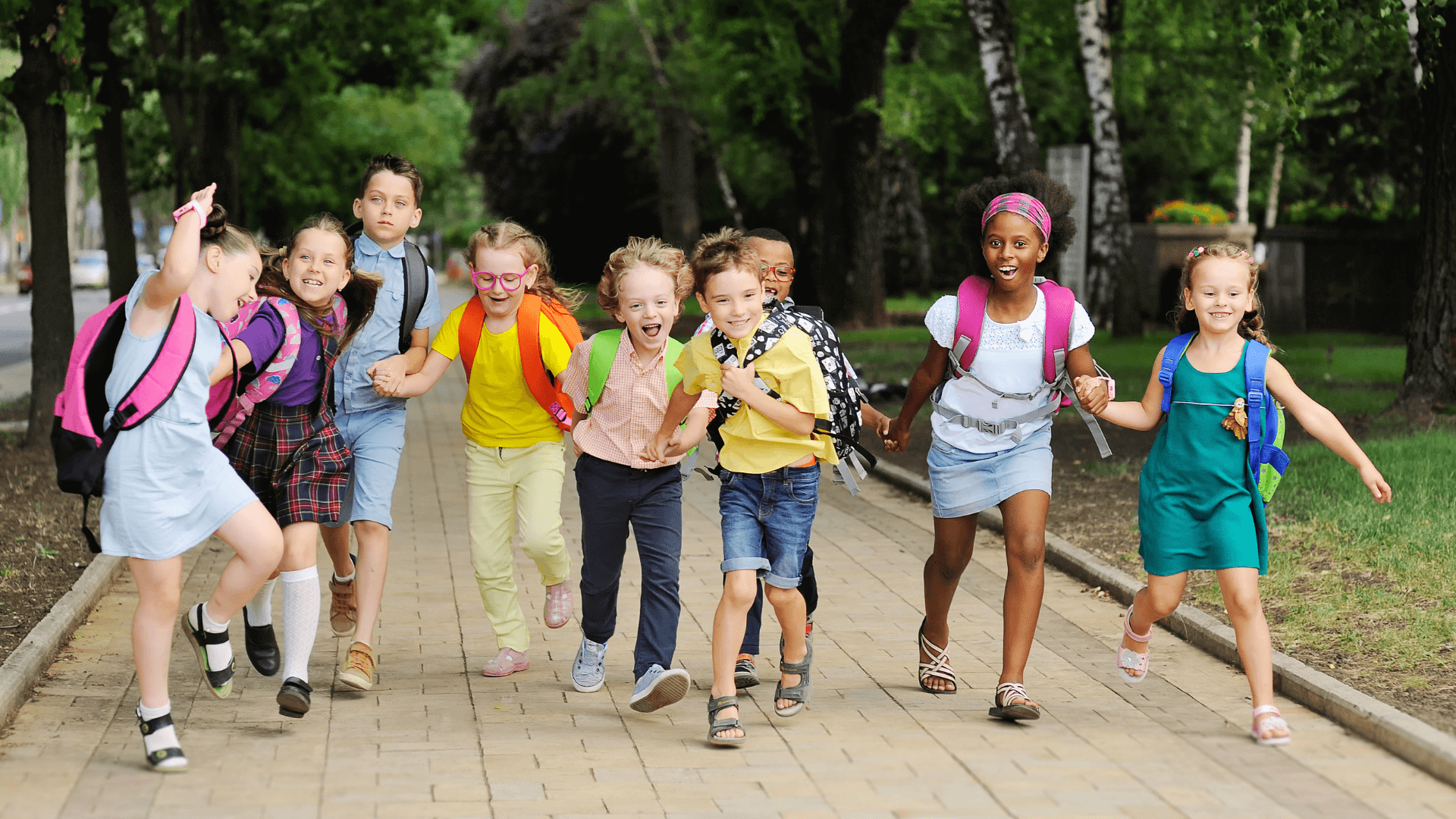 A group of kids with backpacks holding hands and running on a sidewalk